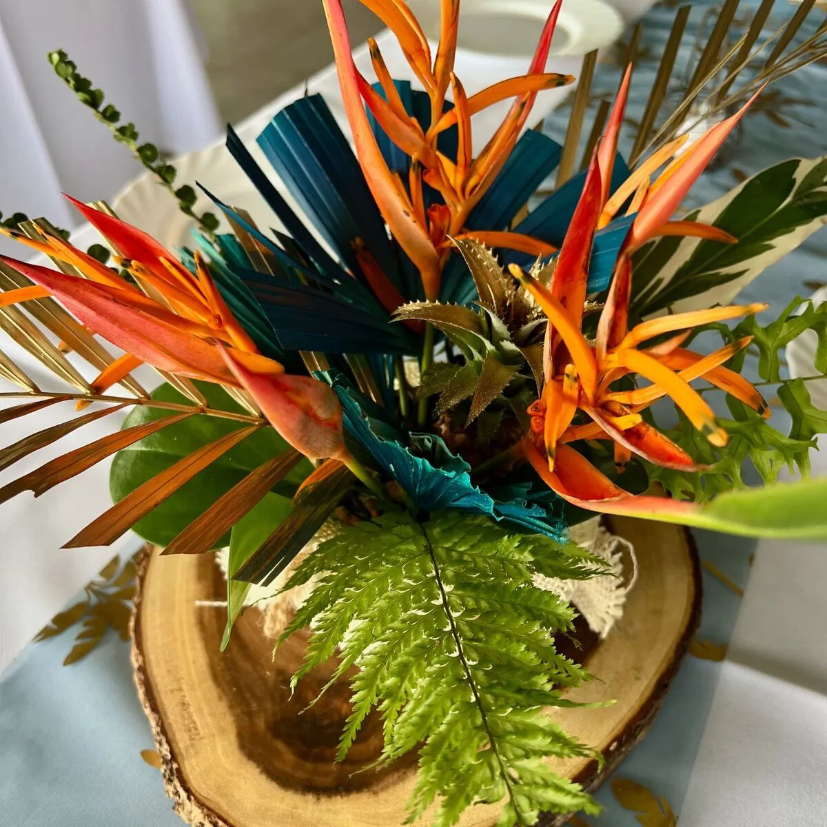 Centre de table tropical avec fleurs oiseaux de paradis, feuillages vert bleu et or sur rondin de bois en Martinique